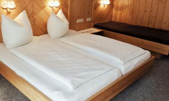 A cozy bedroom with a double bed and a single lounge chair. The walls are made of wood, and there is soft lighting.