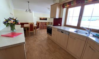 A modern kitchen with wooden cabinets and a large window. There are chairs at the table and a flower vase creates an inviting atmosphere.