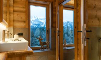 A modern wooden bathroom with large windows and a view of the mountains. It is brightly and cozily furnished.