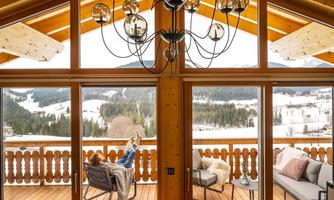 A cozy apartment with large windows and a view of a snow-covered landscape. A person is relaxing in an armchair on the terrace.