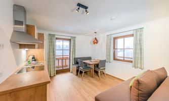 A modern kitchen with wooden furniture and a dining table. Large windows let in plenty of daylight.