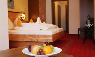 A cozy hotel room with a double bed and warm colors. On a table, there is a bowl of fresh fruit.