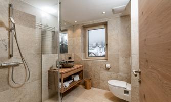 A modern bathroom with sleek tiles and a glass shower. The window offers a view of the winter landscape.