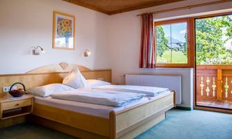 A cozy bedroom with a double bed and a window that overlooks a balcony. The walls are light and there is a beautiful wooden ceiling.