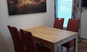 A cozy dining area with a wooden table and four red chairs. A picture of deer in a forest landscape hangs on the wall.