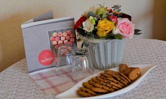 A beautiful table with a surface full of cookies and a glass. Next to it is a floral arrangement and a menu.