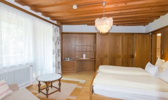 A modern room with a wooden ceiling and large windows. There is a double bed, a cozy seating area, and a beautiful table.