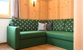 A cozy green couch with an animal pattern and decorative cushions. The room has wooden paneling and windows with curtains.