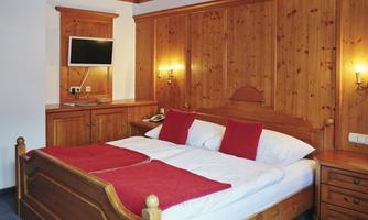 A cozy bedroom with a double bed and red pillows. The walls are made of wood, and there is a TV as well as nightstands.