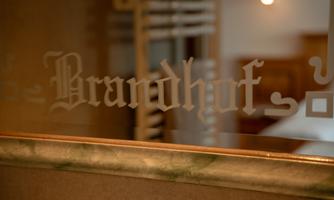 A glass with the inscription "Brandhof". In the background, some details of a room are visible.