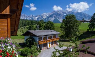 A picturesque landscape with a traditional house and beautiful flowers. In the background, majestic mountains and a clear blue sky can be seen.