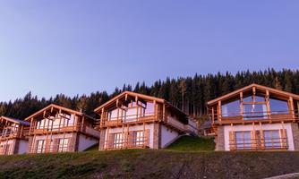 Modern wooden houses in a picturesque mountain landscape. In the background, tall trees and a clear sky are visible.