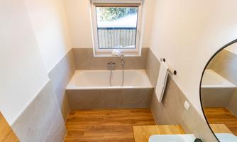 A modern bathroom with a bathtub and a window. The floor is made of wood and there is a sink with a mirror.