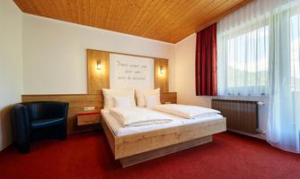 A cozy bedroom with a wooden double bed and a modern armchair. Large windows let in plenty of light and create an inviting atmosphere.