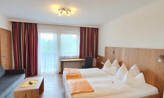 A cozy hotel room with a large double bed and modern furniture. Large windows provide plenty of daylight and a pleasant atmosphere.