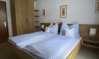 A cozy bedroom with a double bed and striped bedspreads. There are wooden wardrobes and nightstands with lamps.