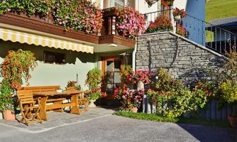 A cozy outdoor area with a wooden table and chairs. Colorful flowers are blooming around the building, creating an inviting atmosphere.