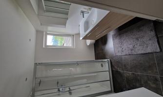 A modern bathroom with a shower and a washbasin. Bright and friendly with a window and neutral colors.