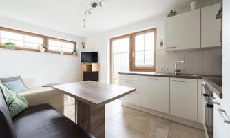 A modern kitchen with a bright ambiance and plenty of natural light. The room features a dining area and a comfortable sofa.