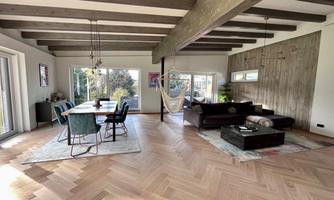 A modern living room with wooden beams and an elegant parquet floor. There is a couch, a coffee table, and a dining area with blue chairs.