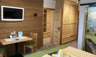 A cozy hotel room with wooden paneling and modern design. There is a table with chairs, a television, and two beds with yellow blankets.