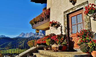 A cozy house with a beautiful entrance and colorful flowers on the porch. In the background, the majestic mountains can be seen.