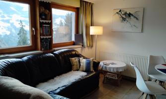 A cozy living area with a black sofa and a small table.  
Large windows offer a view of the surroundings and let in plenty of daylight.