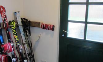 A room with skis stacked against the wall. The door is green and has several windows.