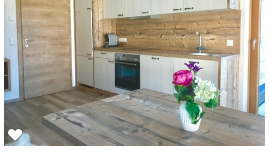 A modern kitchen with bright cabinets and wooden details. On a table, there is a vase with colorful flowers.