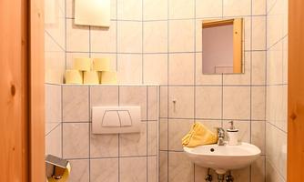 A small bathroom with white tiles and blue floor tiles. It contains a sink, a toilet, and some toiletries.