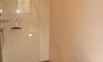 A modern bathroom with a large shower and bright tiles. The floor is in a darker shade.