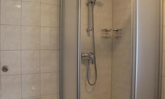 A modern shower cabin with clear glass walls and a handheld showerhead. The floor is tiled and there is a small shelf available.