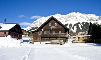 A charming wooden house in a snow-covered village. Impressive mountains and a blue sky can be seen in the background.