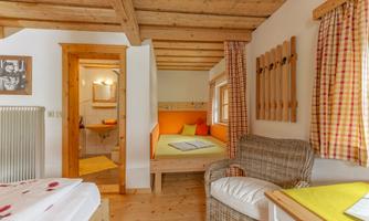 A cozy room in alpine style with wooden ceilings and a pleasant atmosphere. There is a bed, a seating area, and access to a bathroom.