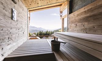A bright sauna with wooden benches and a view of the mountains. The large window allows nature to be seen, creating a relaxing atmosphere.