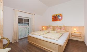 A bright bedroom with a large double bed and wooden paneling. There is a window view and cozy decorations.