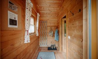 A cozy hallway in a wooden house with wooden walls. The room has a carpet, curtains, and space for clothing.