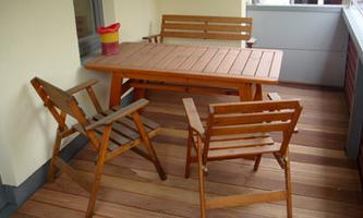A balcony with a wooden dining table and four chairs. The furniture is simple and functional.