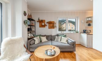 A cozy living room with a gray sofa and a round wooden table. Large windows provide a view of the surrounding mountains, and the decor is modern and inviting.