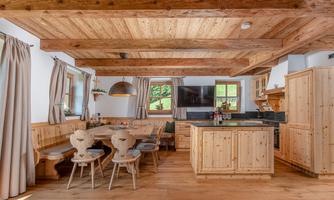 A cozy wooden kitchen with a large dining table and wooden chairs. The windows offer a beautiful view of the outdoors.