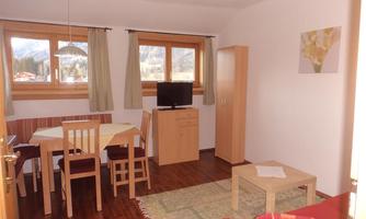 A cozy living area with a dining table and chairs. The room has large windows with a view of the mountains and is simply furnished.
