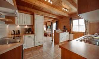 A modern kitchen with wooden beam ceiling and bright furniture. The room has large windows that let in plenty of natural light.