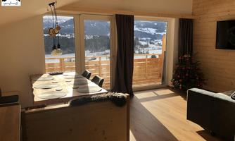 Bright and modern living and dining room with a view of snow-covered mountains. A table and a cozy armchair invite you to relax.
