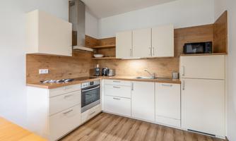 A modern kitchen with bright cabinets and wooden shelves. The space is well-lit and has all the essential appliances.