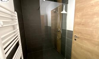A modern bathroom with a shower and a wooden sink. The walls are in dark colors, and the door is made of wood.