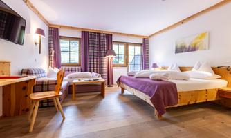 A cozy hotel room with two beds and a table. Large windows let in plenty of light and offer a nice view.
