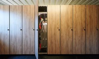 A modern changing room with wooden lockers. One of the lockers is open and shows the items stored inside.