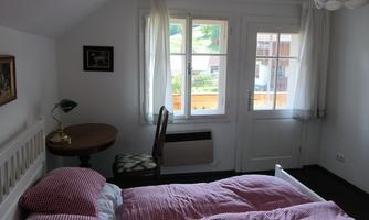 A cozy bedroom with a double bed and a small table. Large windows let in plenty of light and offer a view outside.