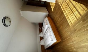 A cozy bedroom with a double bed and light wooden floor. The room is well-lit and has a relaxed atmosphere.