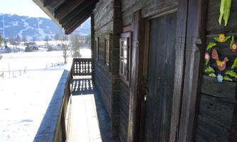 A rustic wooden house with a porch, surrounded by snow-covered landscapes. In the background, mountains can be seen.